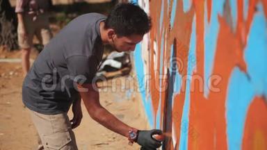 涂鸦艺术家在街墙上画画。 帅气的男人用喷雾瓶喷着五颜六色的油漆，城市